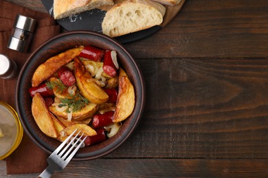 Photo of Delicious baked potato with thin dry smoked sausages in bowl served on wooden table, flat lay. Space for text