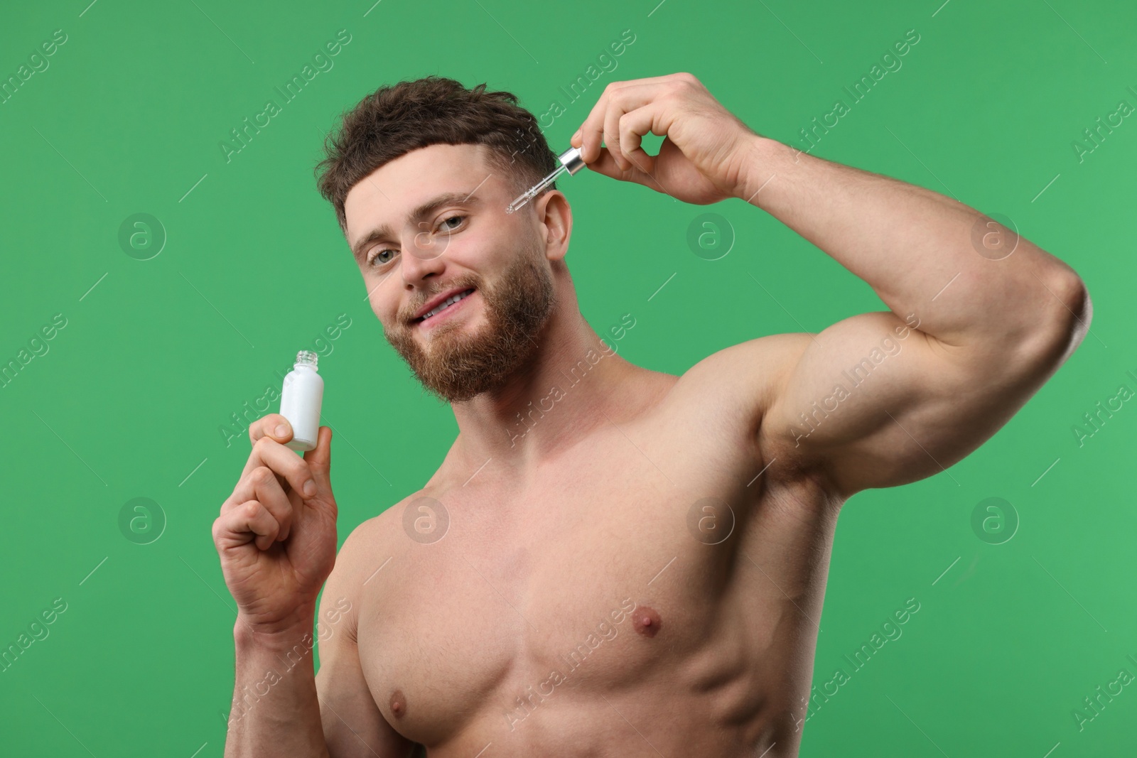 Photo of Handsome man applying serum onto his face on green background