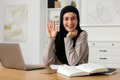 Photo of Muslim woman working near laptop at wooden table in room