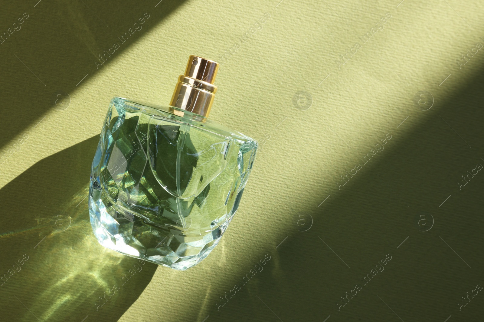 Photo of Luxury women's perfume. Sunlit glass bottle on olive background, top view. Space for text