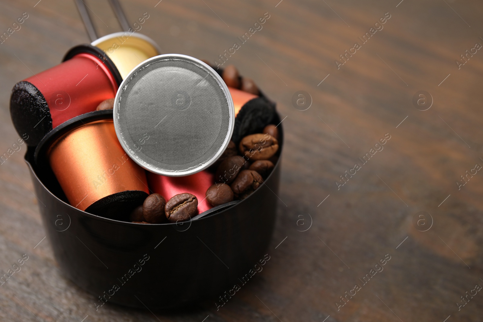 Photo of Saucepan with coffee capsules and beans on wooden table, closeup. Space for text