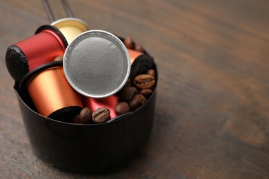 Saucepan with coffee capsules and beans on wooden table, closeup. Space for text