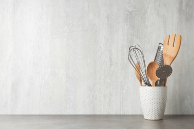 Holder with kitchen utensils on grey table against light background. Space for text