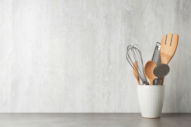 Photo of Holder with kitchen utensils on grey table against light background. Space for text