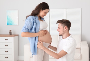Young husband touching his pregnant wife's tummy at home