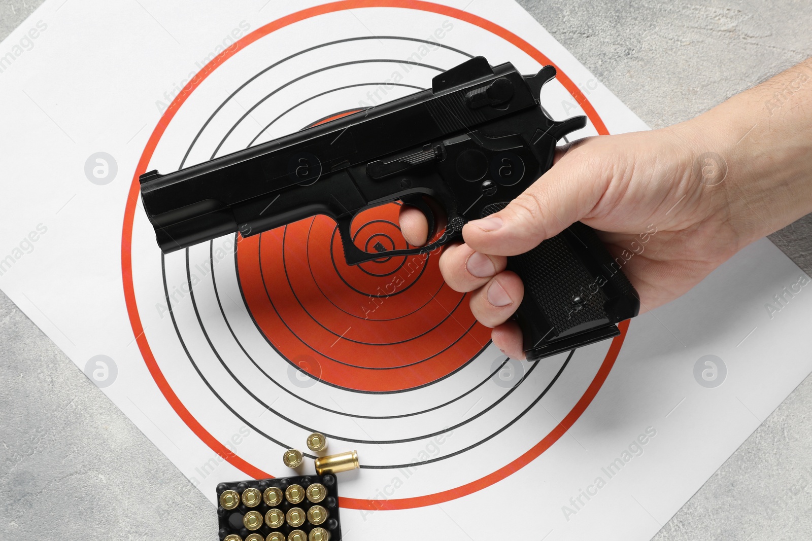 Photo of Man with handgun, shooting target and bullets at gray table, top view