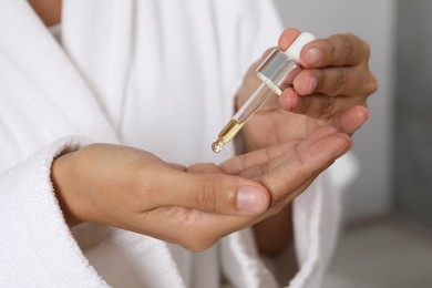 Photo of Woman applying cosmetic serum onto her hand on blurred background, closeup