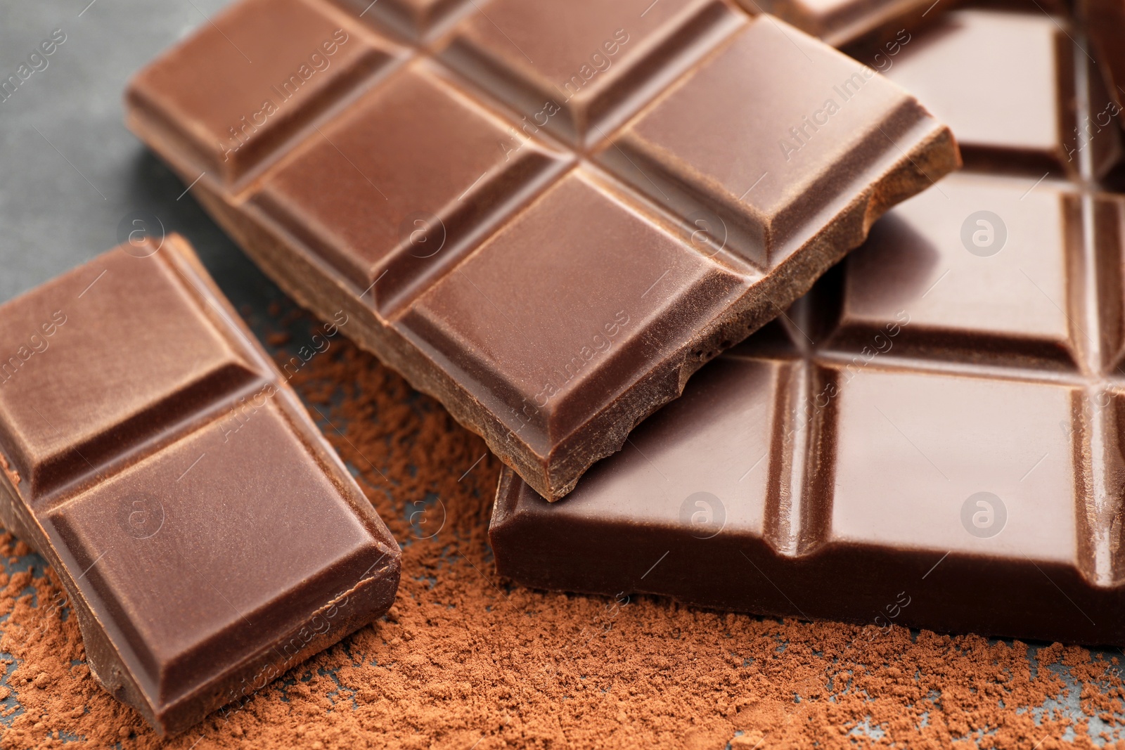 Photo of Delicious dark chocolate and cocoa powder on black table, closeup