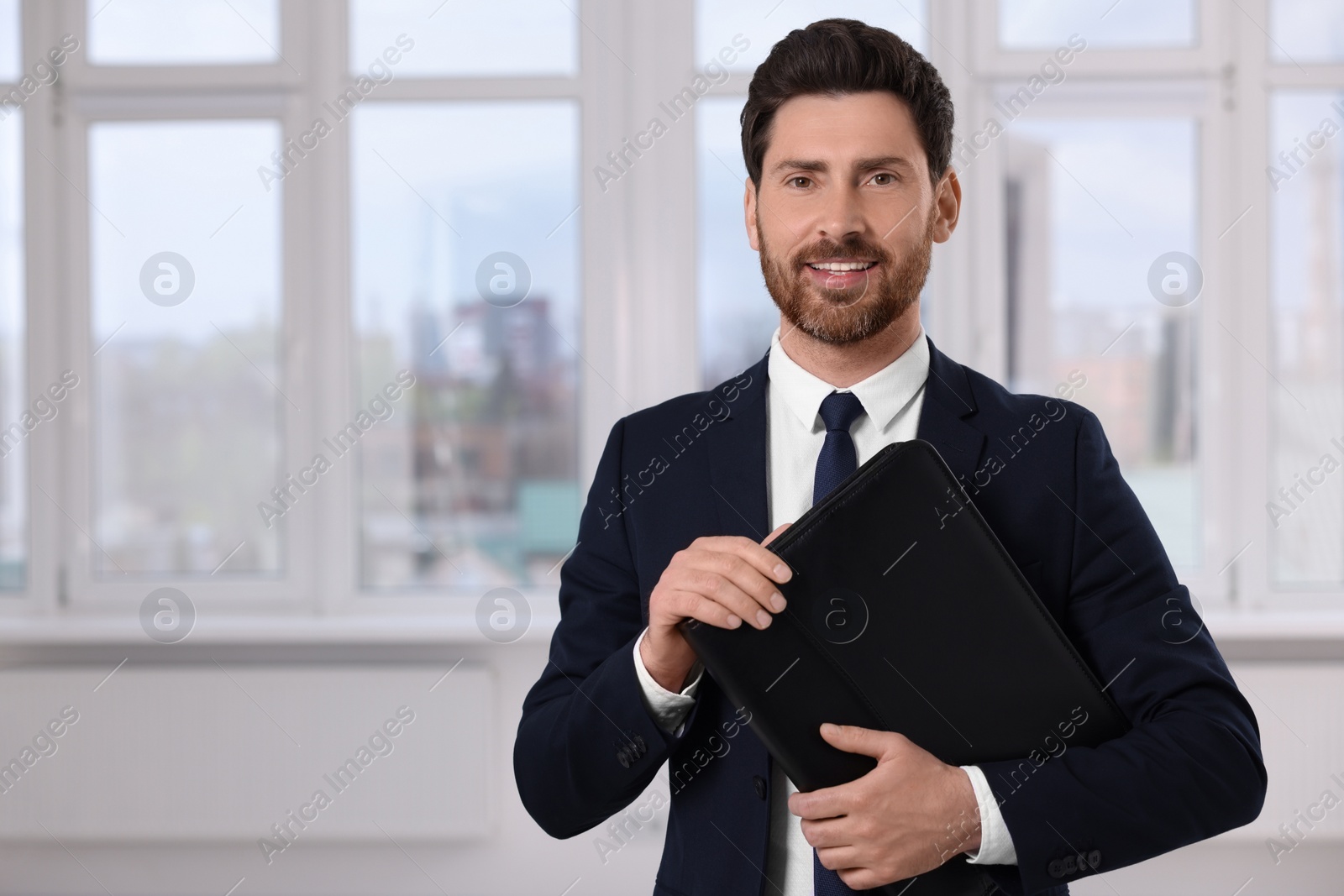 Photo of Happy real estate agent with leather portfolio indoors. Space for text