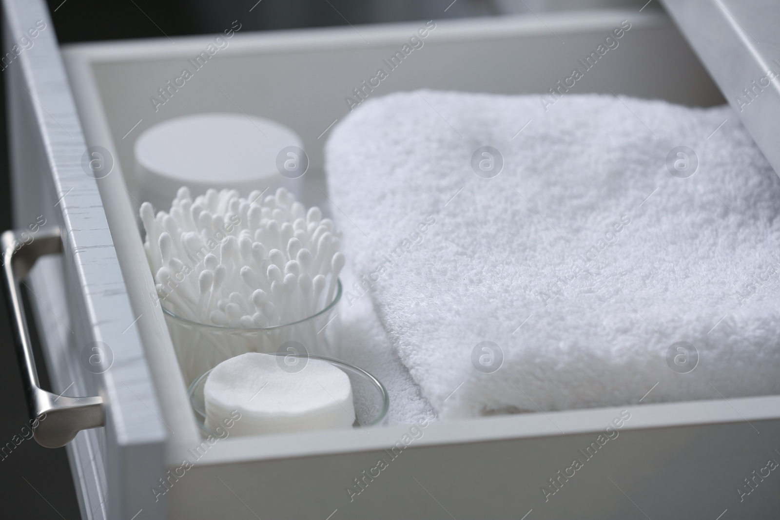 Photo of Open cabinet drawer with cotton buds, pads and towels indoors, closeup