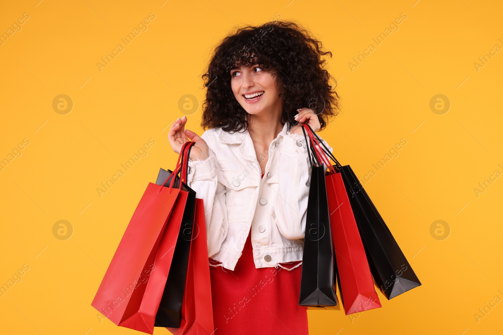 Photo of Happy young woman with shopping bags on yellow background