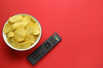 Photo of Remote control and bowl of potato chips on red background, flat lay. Space for text