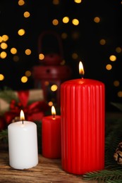 Photo of Burning candles and Christmas decor on wooden table against blurred festive lights