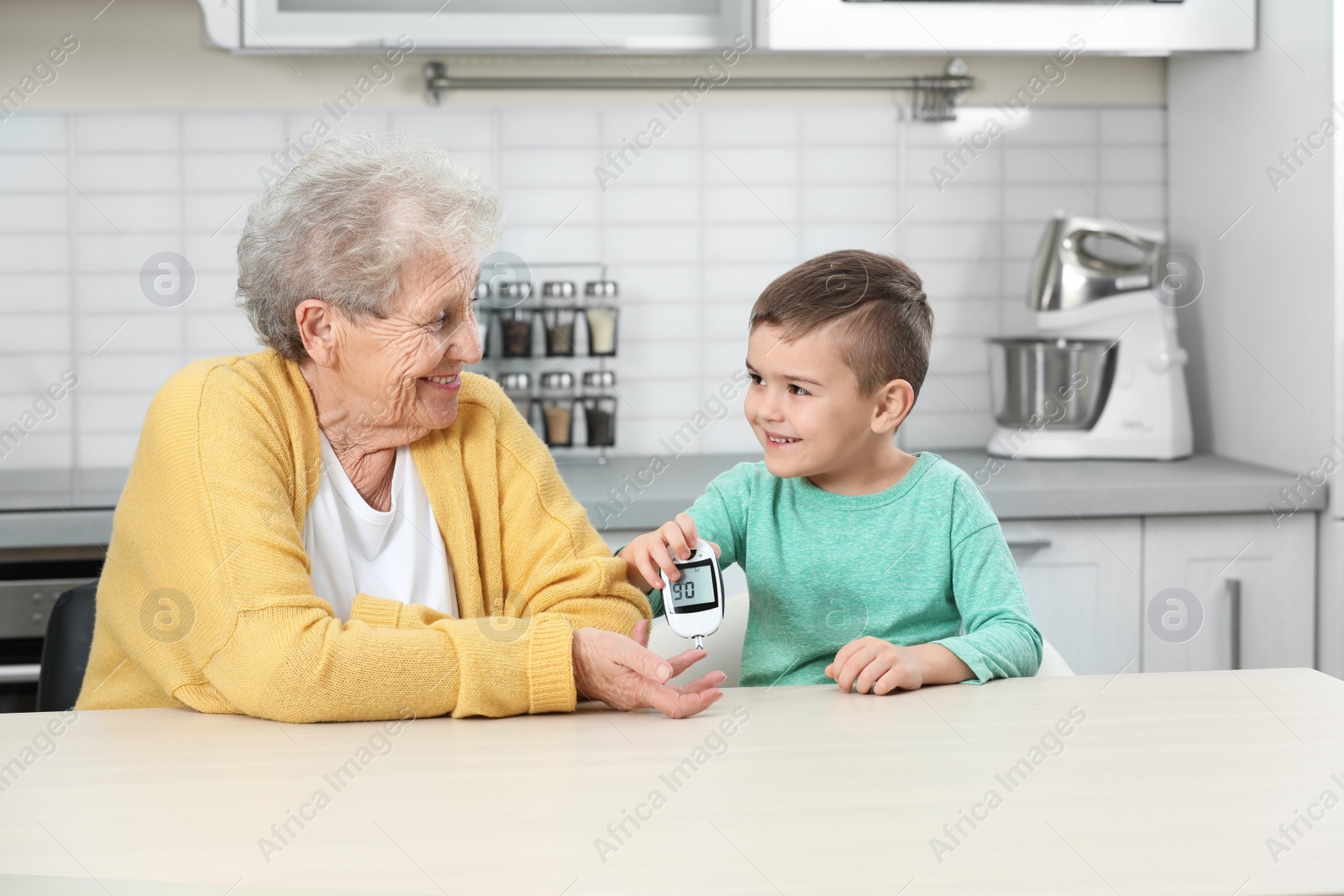 Photo of Senior woman with her grandson using digital glucometer at home. Diabetes control