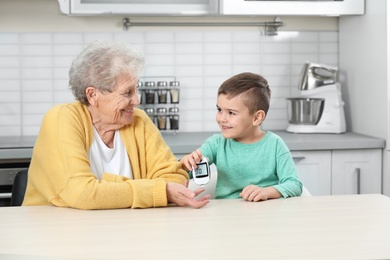 Senior woman with her grandson using digital glucometer at home. Diabetes control