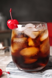 Tasty cola with ice cubes and cherry on table, closeup