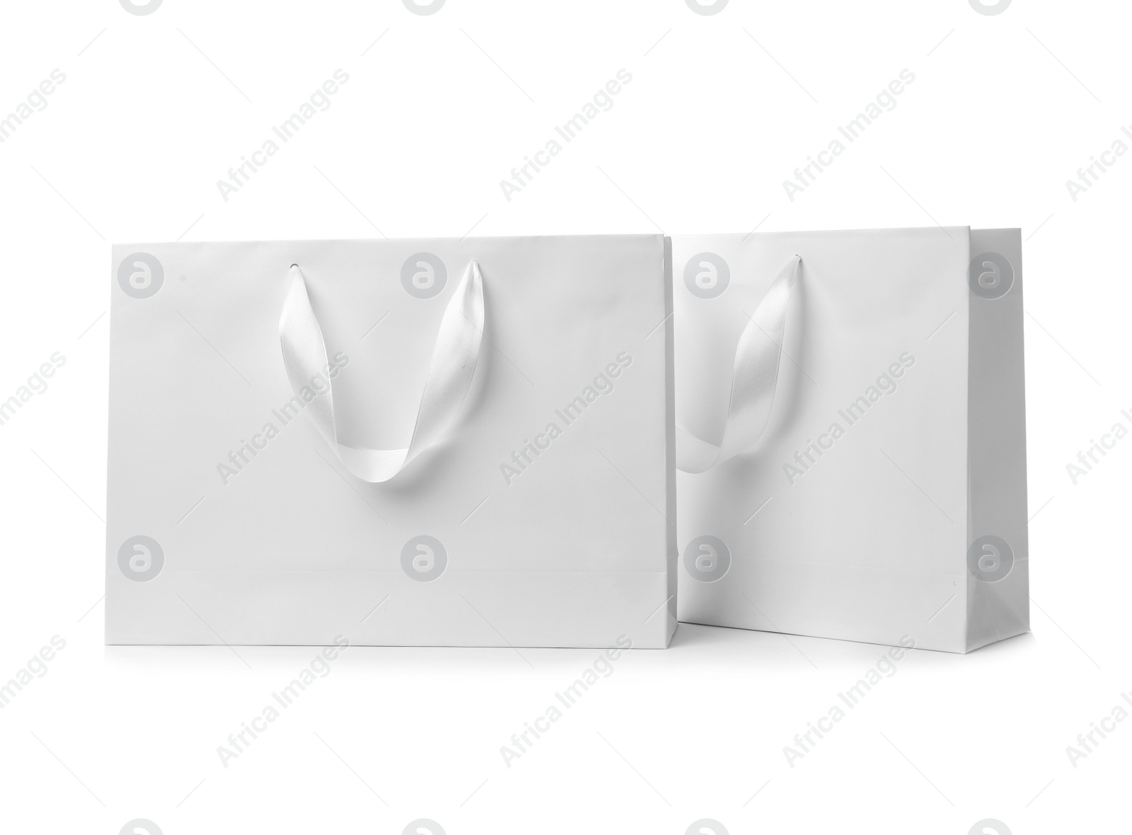 Photo of Paper shopping bags with ribbon handles on white background. Mockup for design