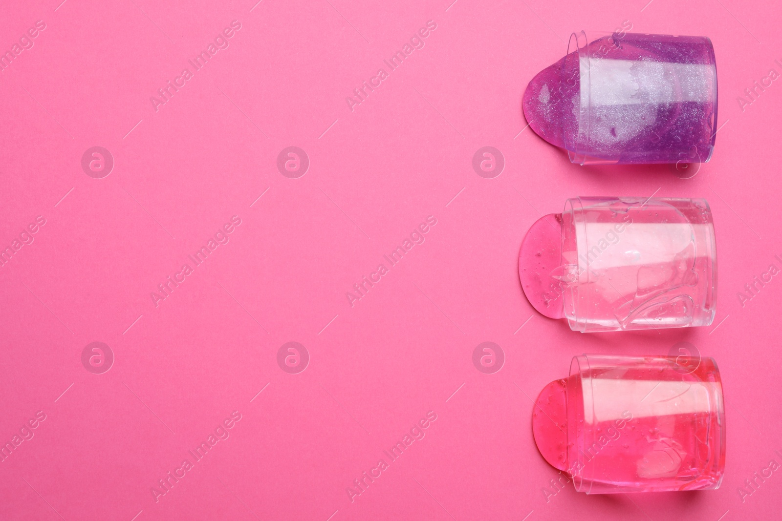 Photo of Overturned plastic containers with bright slimes on pink background, top view. Space for text