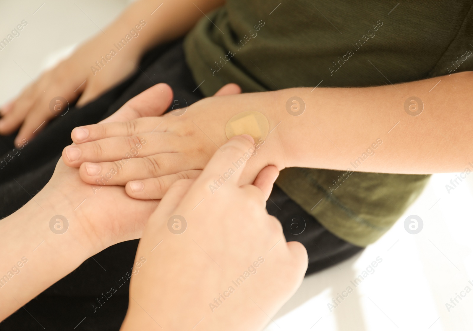 Photo of Sister putting sticking plaster onto little brother's hand indoors, closeup