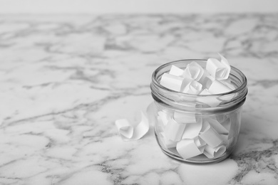 Photo of Glass jar with paper pieces on white marble table, space for text