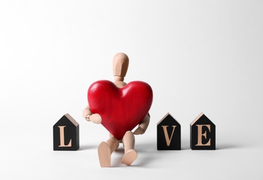 Word Love made of decorative letters, wooden mannequin and red heart on white background