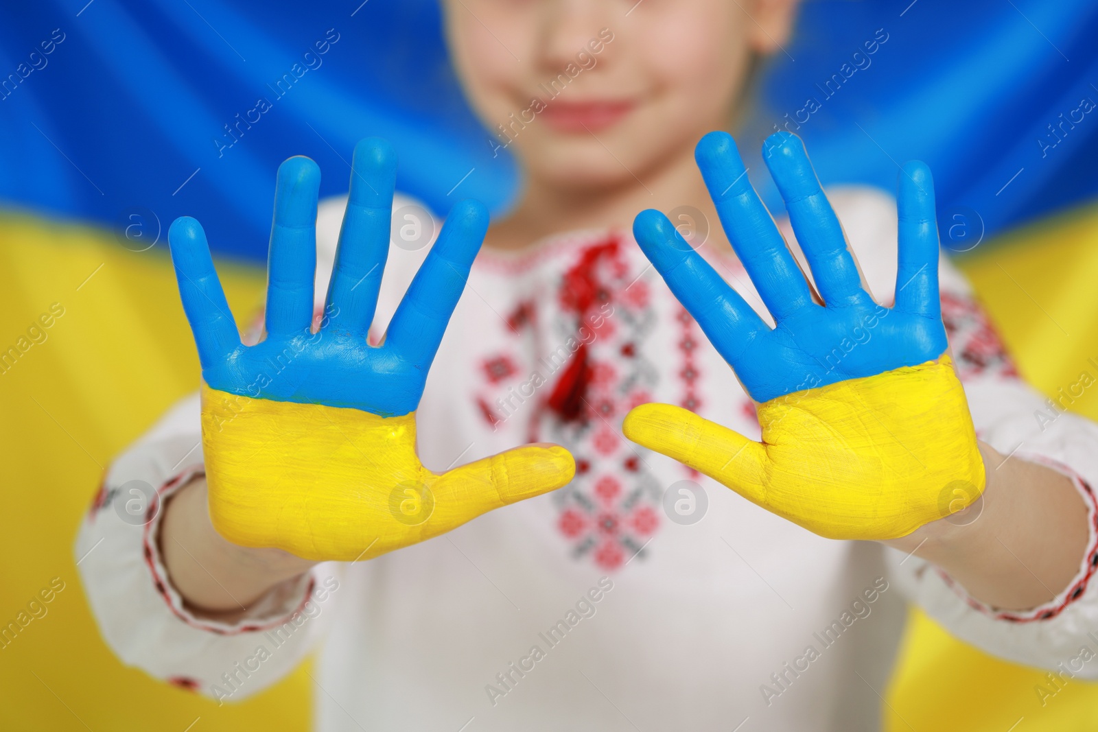 Photo of Little girl with painted hands near Ukrainian flag, closeup. Love Ukraine concept