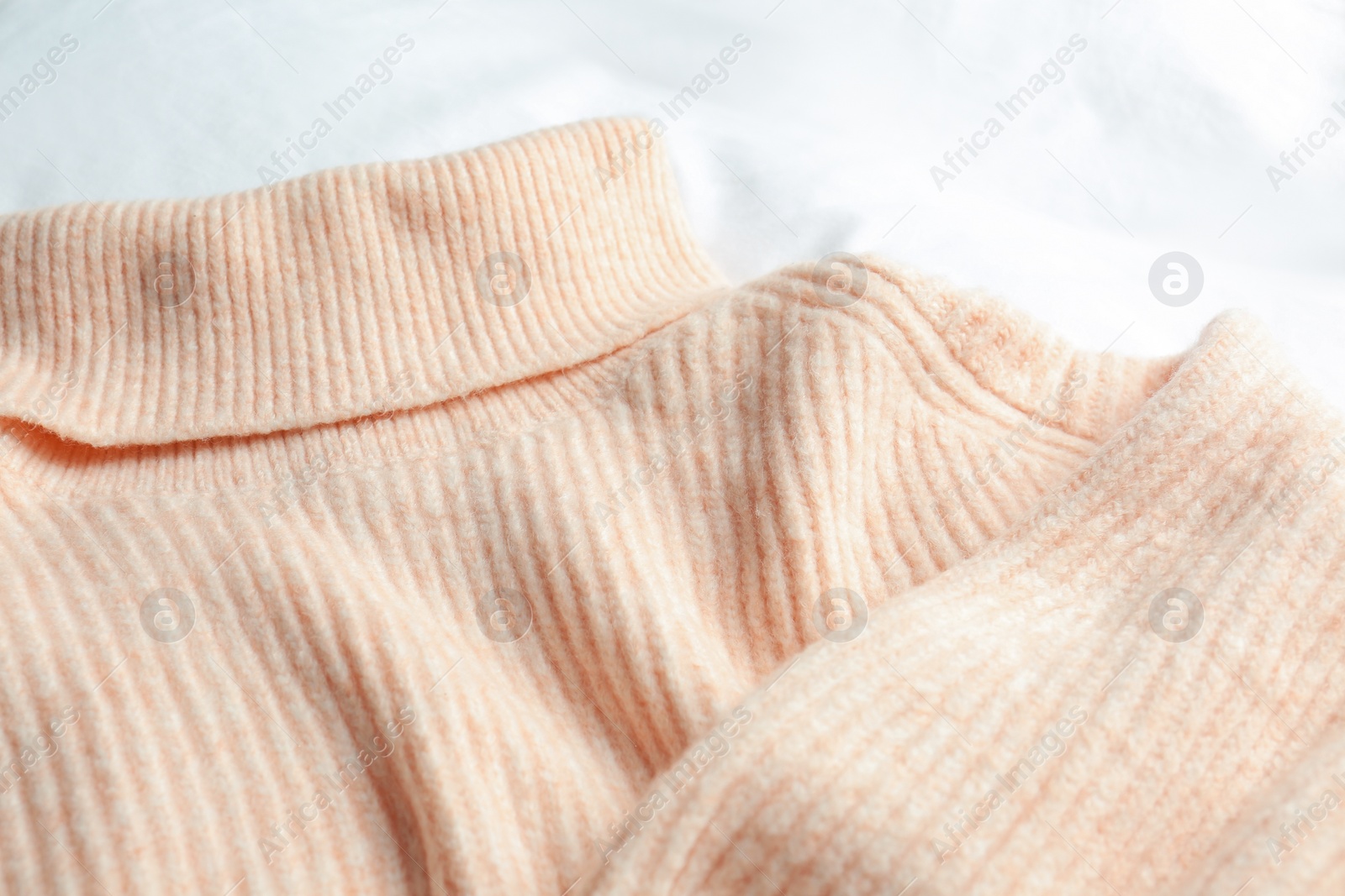 Photo of Stylish knitted sweater on white fabric, closeup