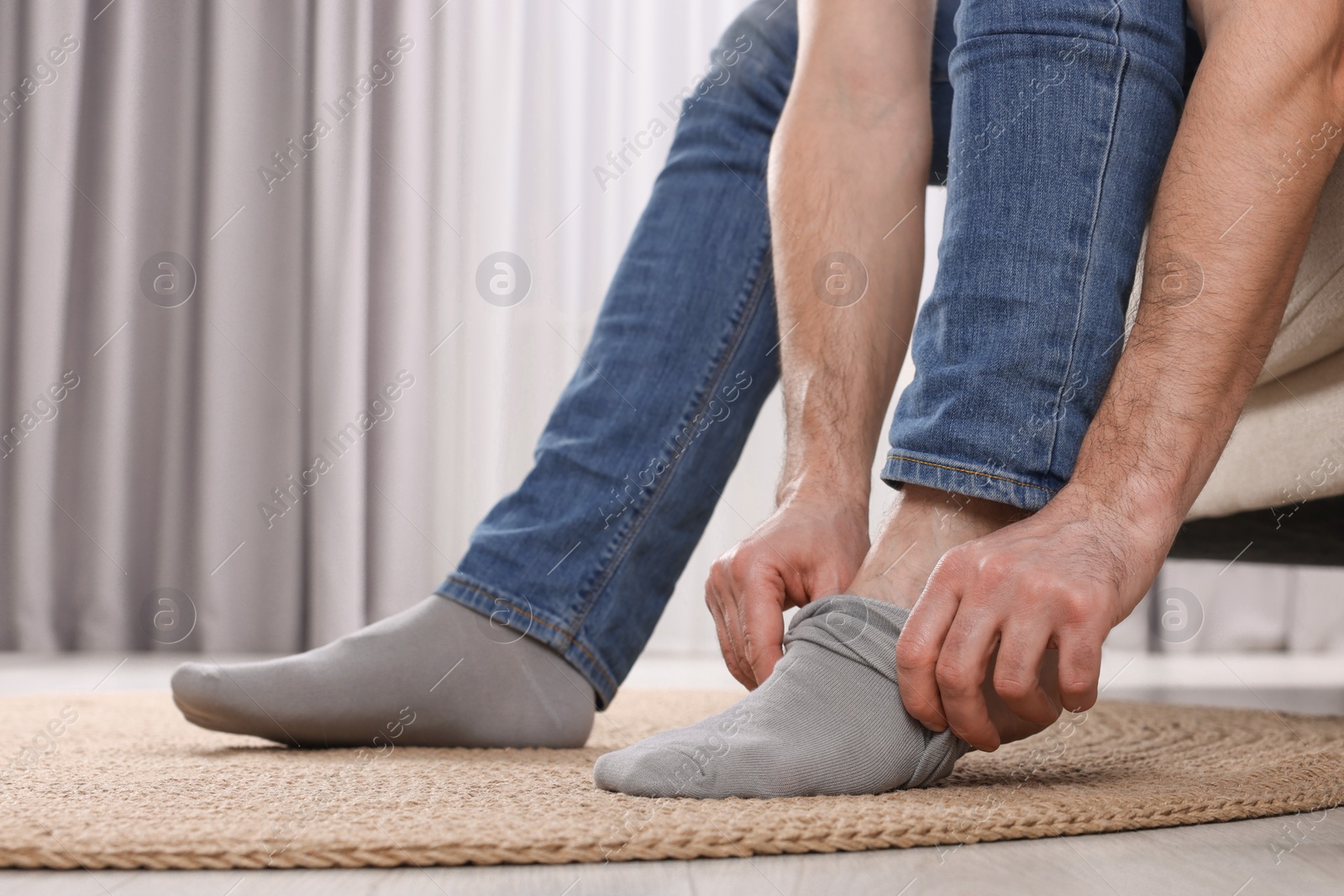 Photo of Man putting on grey socks at home, closeup