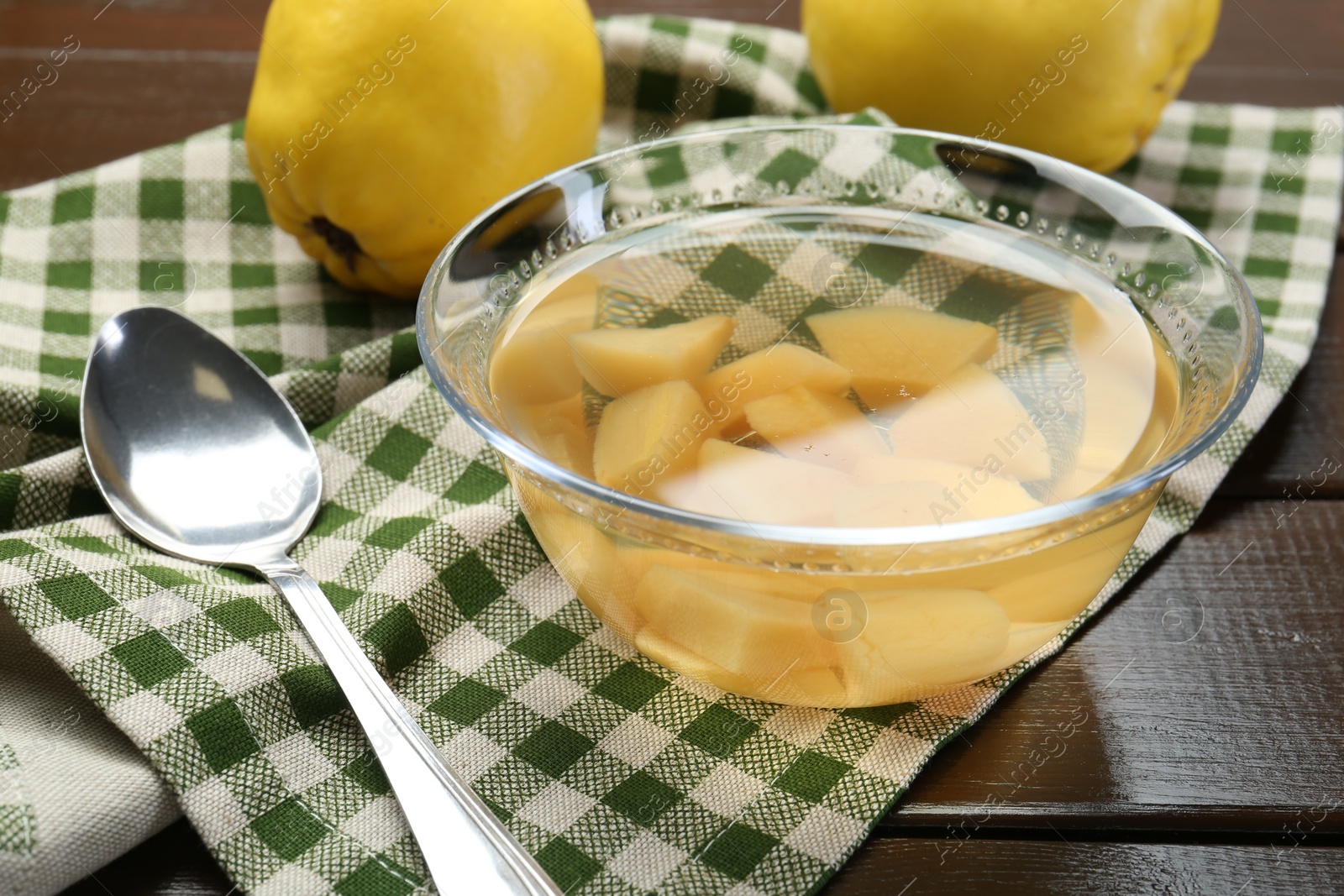 Photo of Delicious quince drink in glass bowl, fresh fruits and spoon on wooden table, closeup