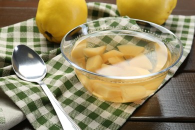 Photo of Delicious quince drink in glass bowl, fresh fruits and spoon on wooden table, closeup