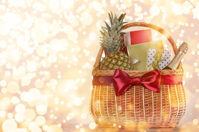 Image of Wicker basket with gifts, champagne and food against blurred festive lights. Space for text