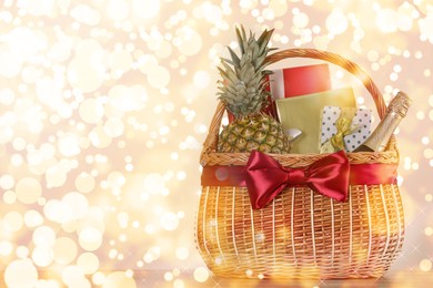 Wicker basket with gifts, champagne and food against blurred festive lights. Space for text