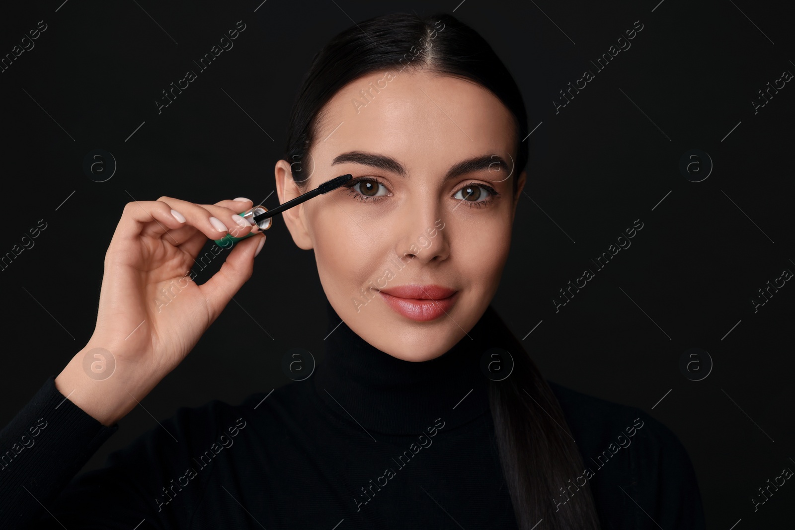 Photo of Beautiful young woman applying mascara on black background