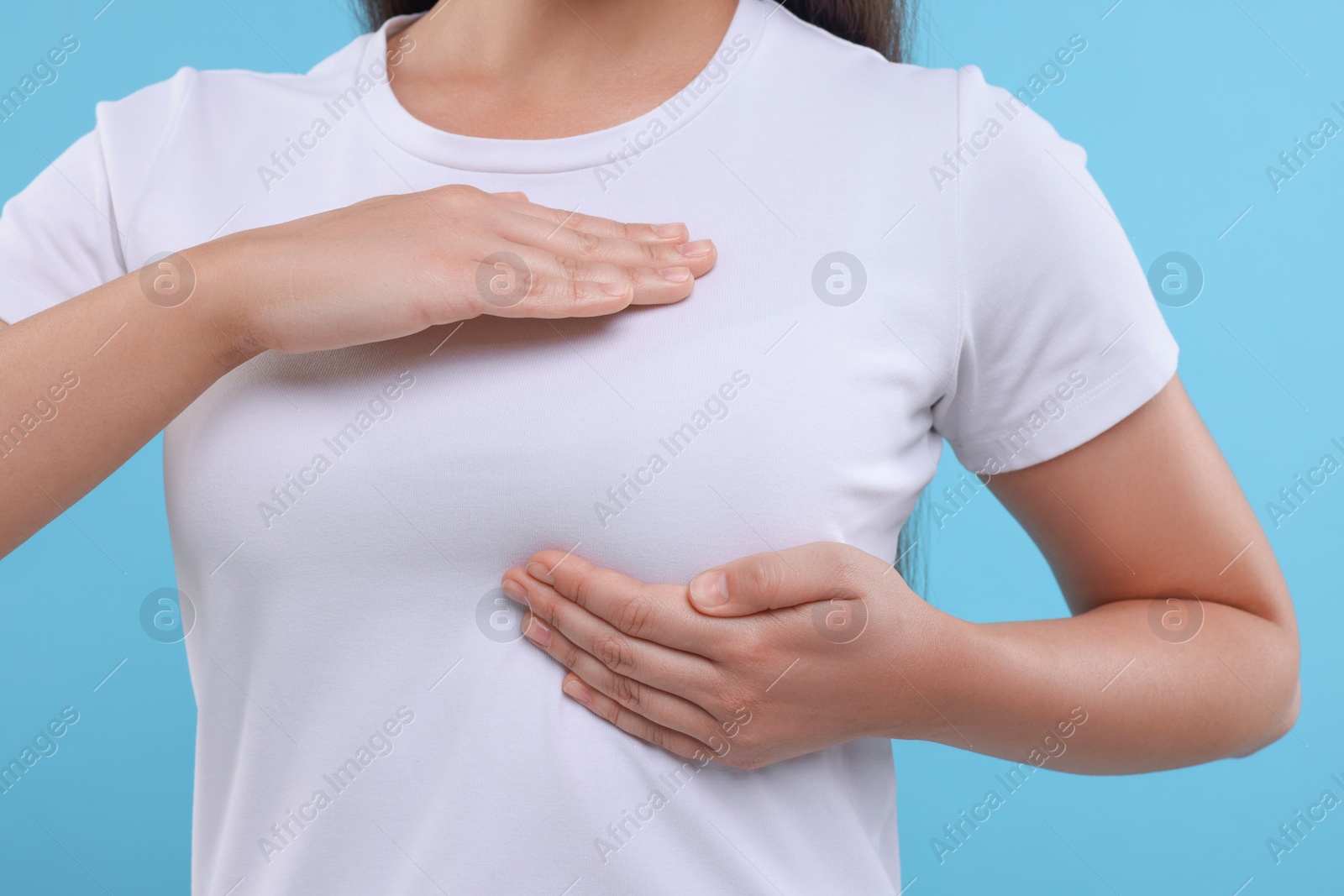 Photo of Woman doing breast self-examination on light blue background, closeup