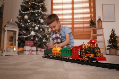 Photo of Little boy playing with colorful toy in room decorated for Christmas, focus on train