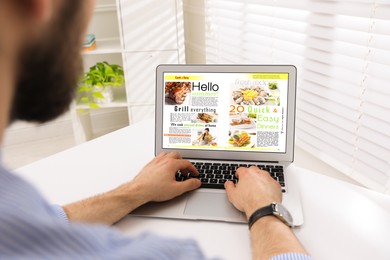 Photo of Man reading online magazine on laptop at white table, closeup