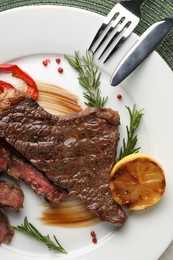Photo of Delicious grilled beef steak with pepper, spices and lemon served on table, top view