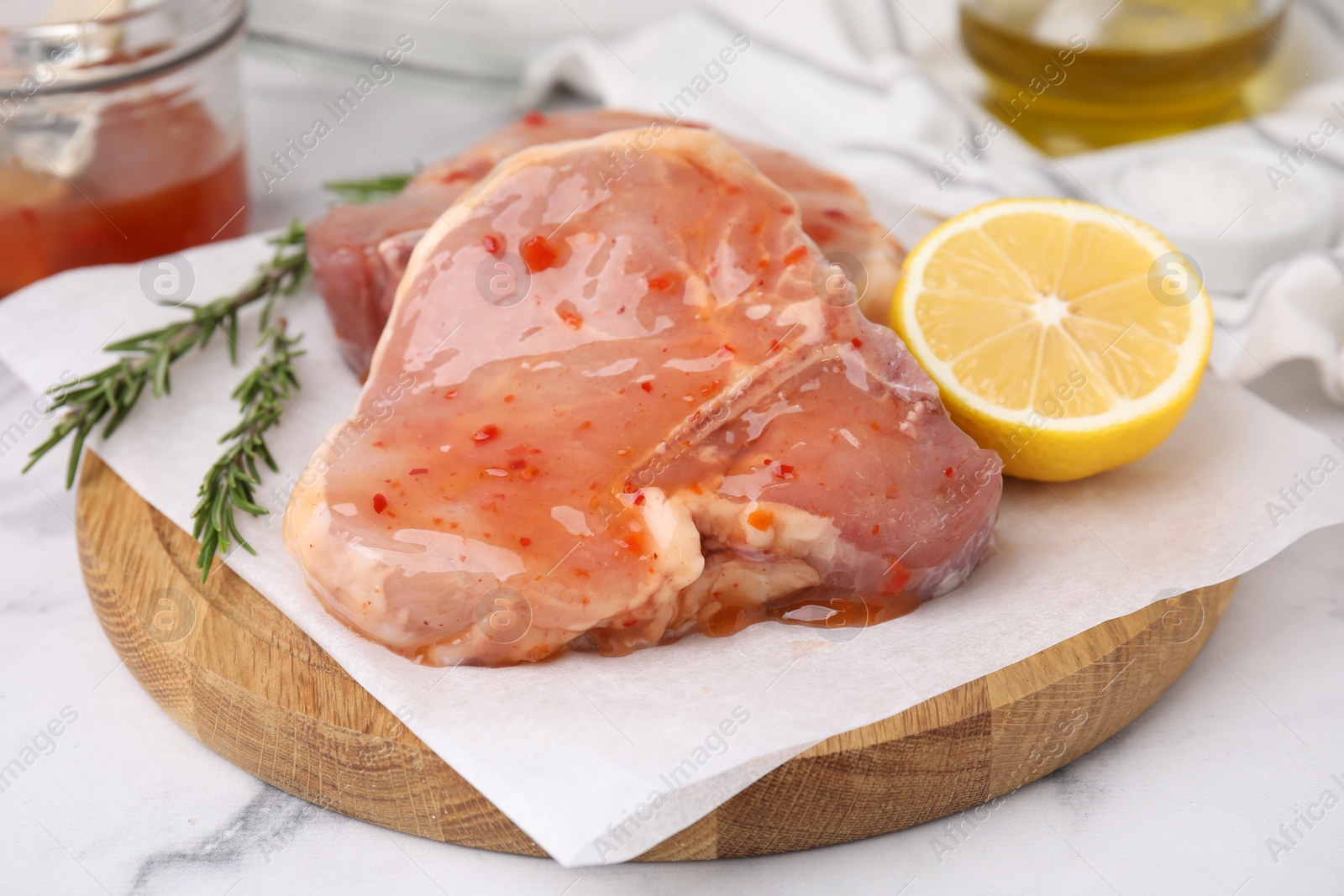 Photo of Board with raw marinated meat, lemon and rosemary on white marble table, closeup