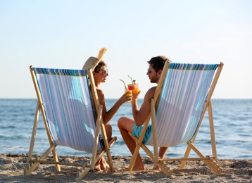 Photo of Young couple with cocktails in beach chairs at seacoast
