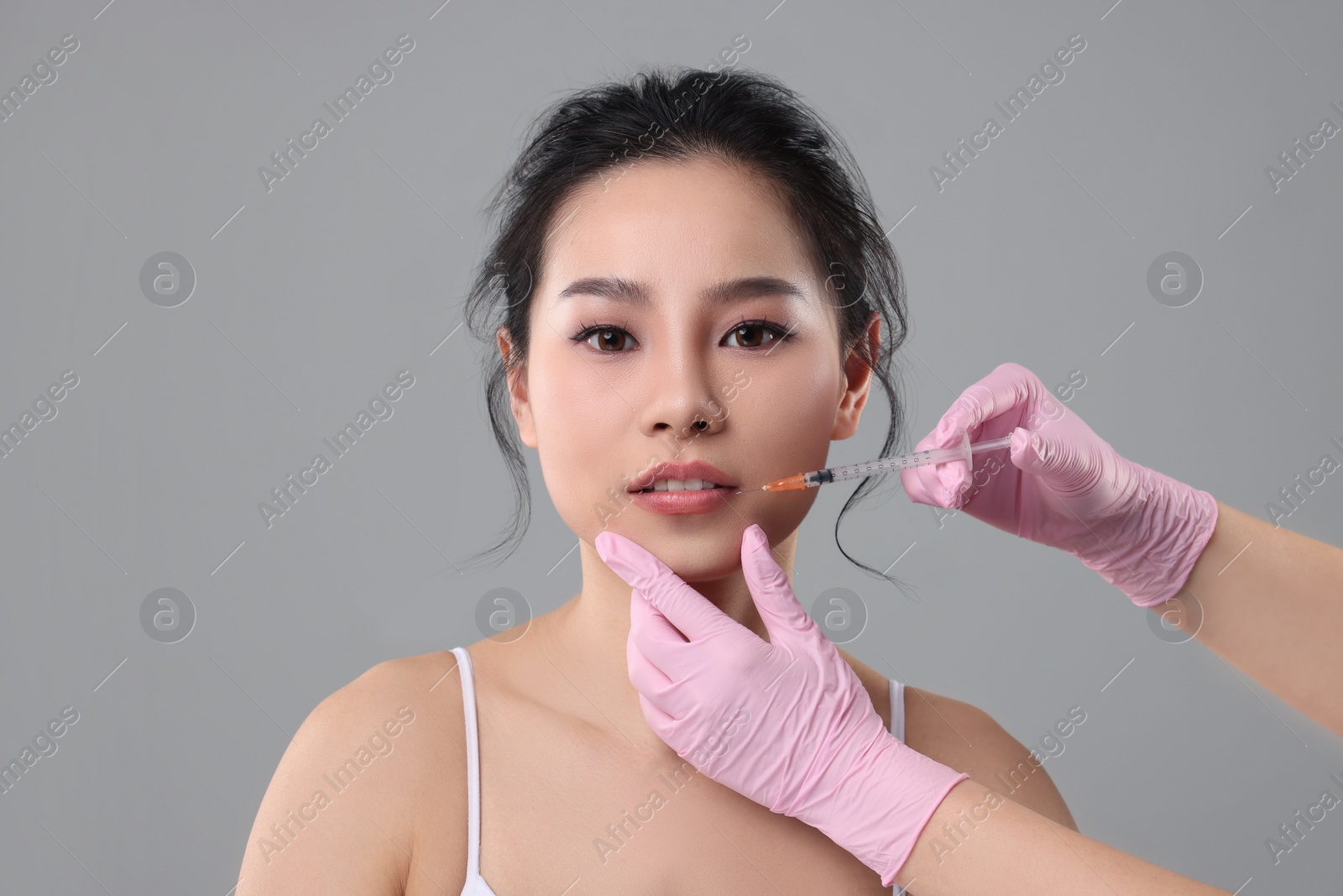 Photo of Woman getting lip injection on grey background