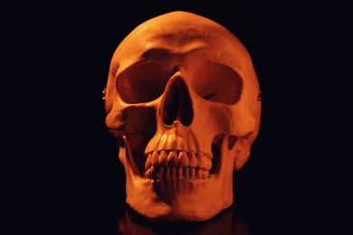 Photo of Orange human skull with teeth on black background