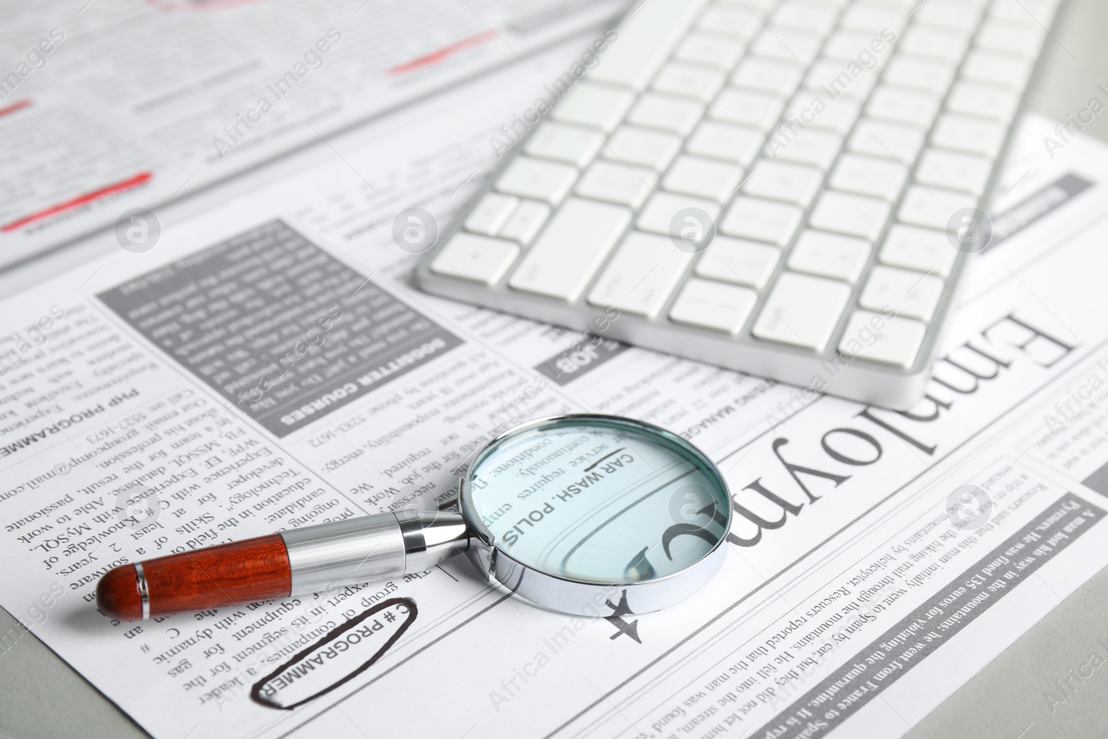 Photo of Magnifying glass and keyboard on newspaper. Job search concept