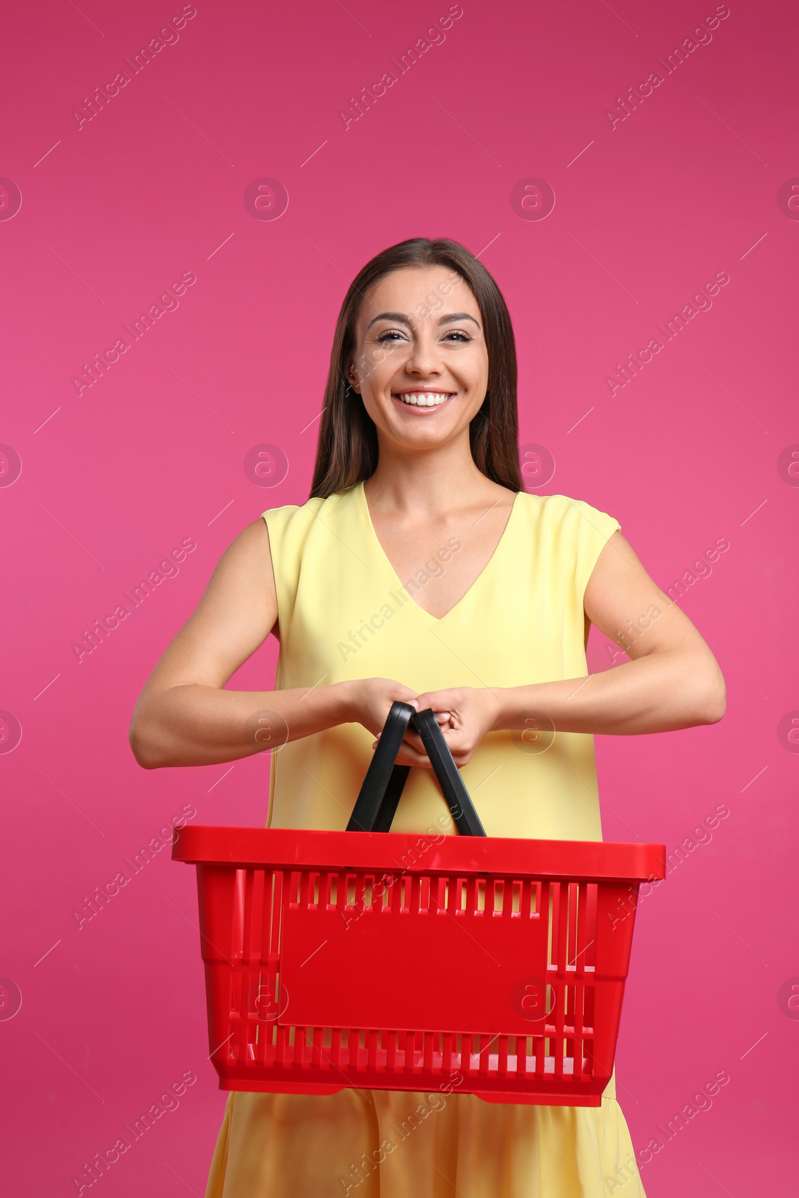 Photo of Young woman with empty shopping basket on pink background