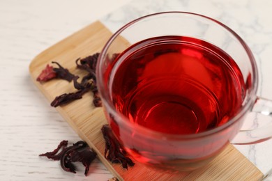 Photo of Cup of fresh hibiscus tea and dry flower leaves on wooden table, closeup