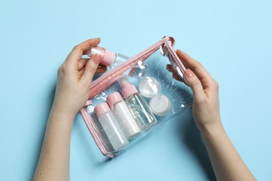 Photo of Cosmetic travel kit. Woman putting small bottle with personal care product into plastic bag against light blue background, top view