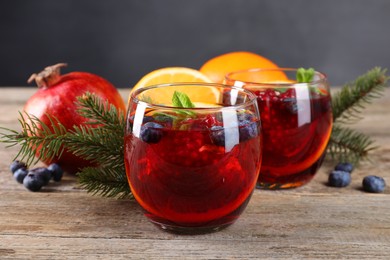 Photo of Aromatic Christmas Sangria drink in glasses, fir branches and ingredients on wooden table