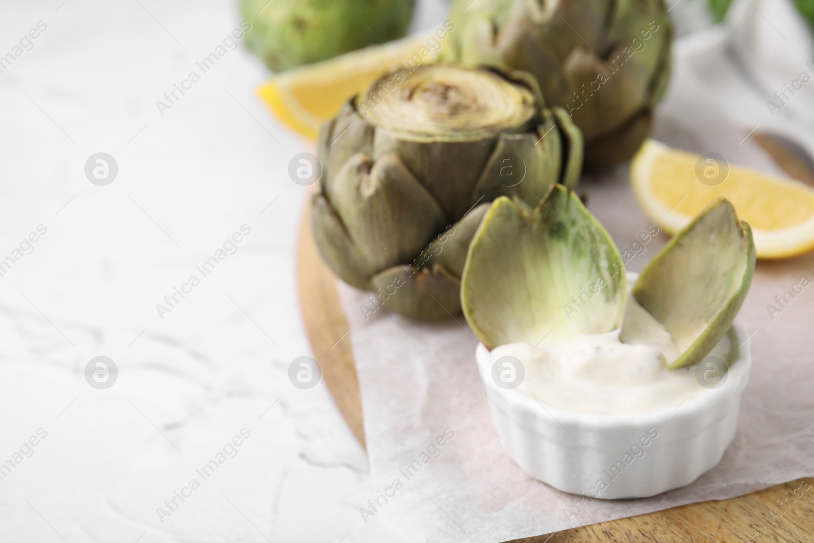 Photo of Delicious cooked artichoke with tasty sauce on white textured table, closeup. Space for text