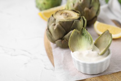 Delicious cooked artichoke with tasty sauce on white textured table, closeup. Space for text