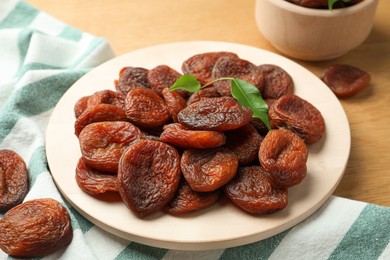 Photo of Plate of tasty apricots and green leaves on wooden table. Dried fruits
