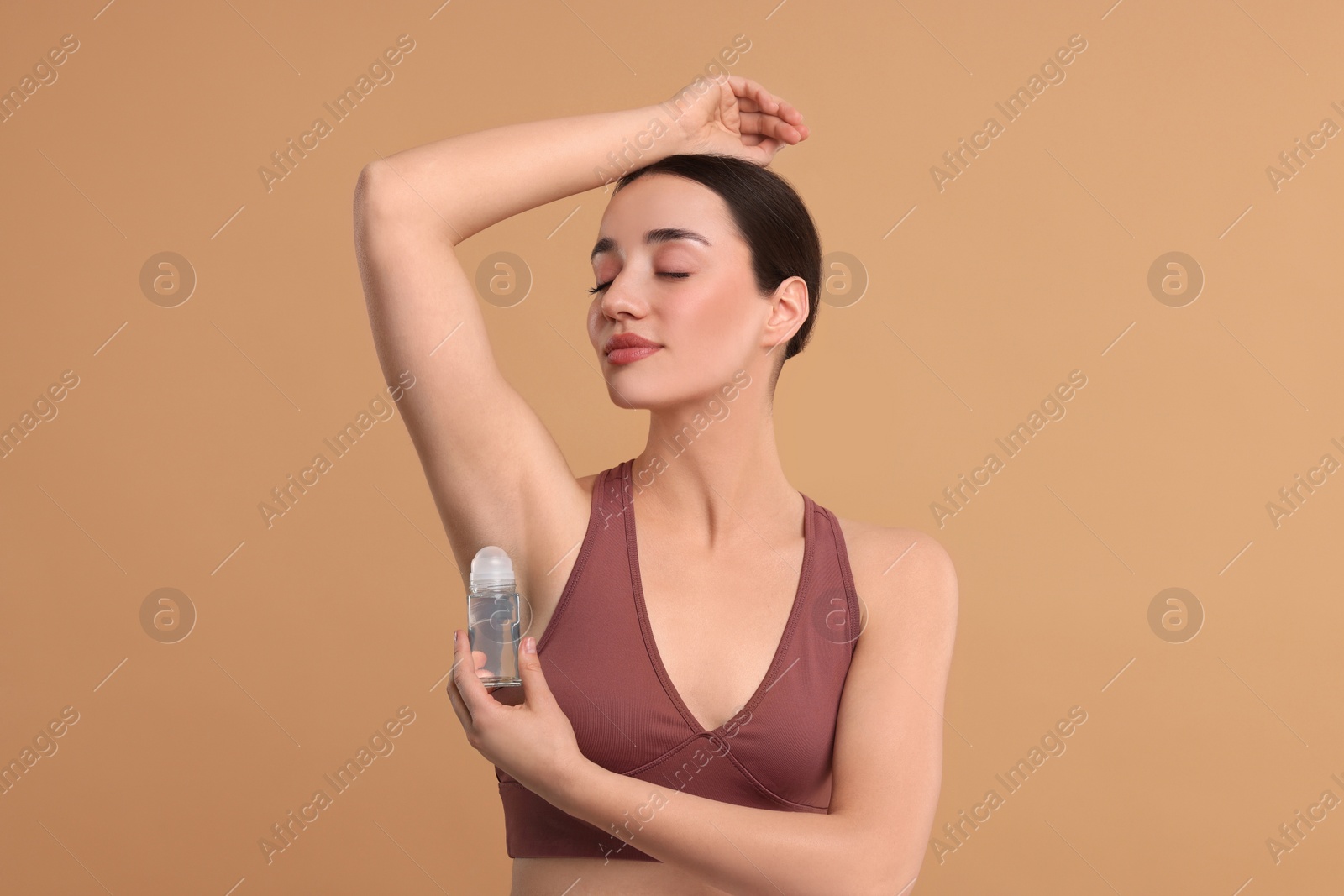 Photo of Beautiful woman applying deodorant on beige background